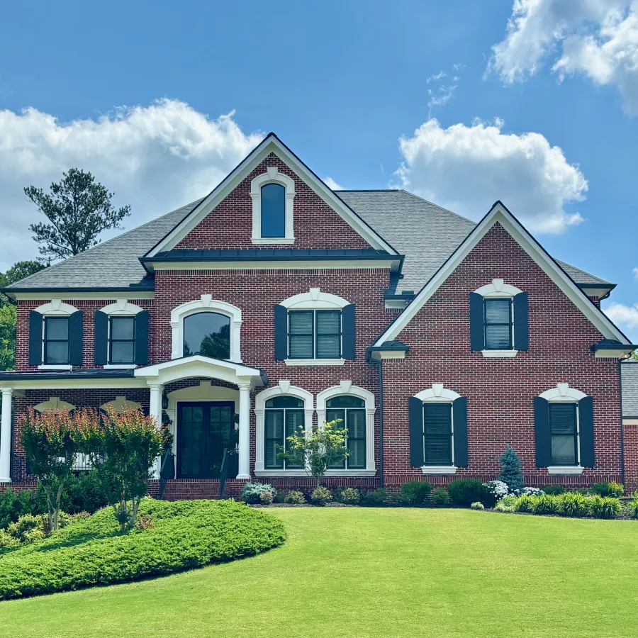 Elegant brick house with lush green lawn under a sunny blue sky with fluffy clouds.
