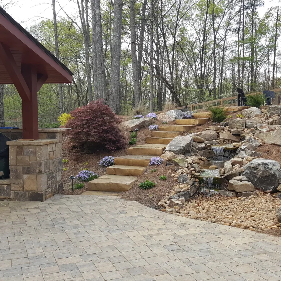 a stone patio with a brick wall and a brick walkway with a building and trees in the background