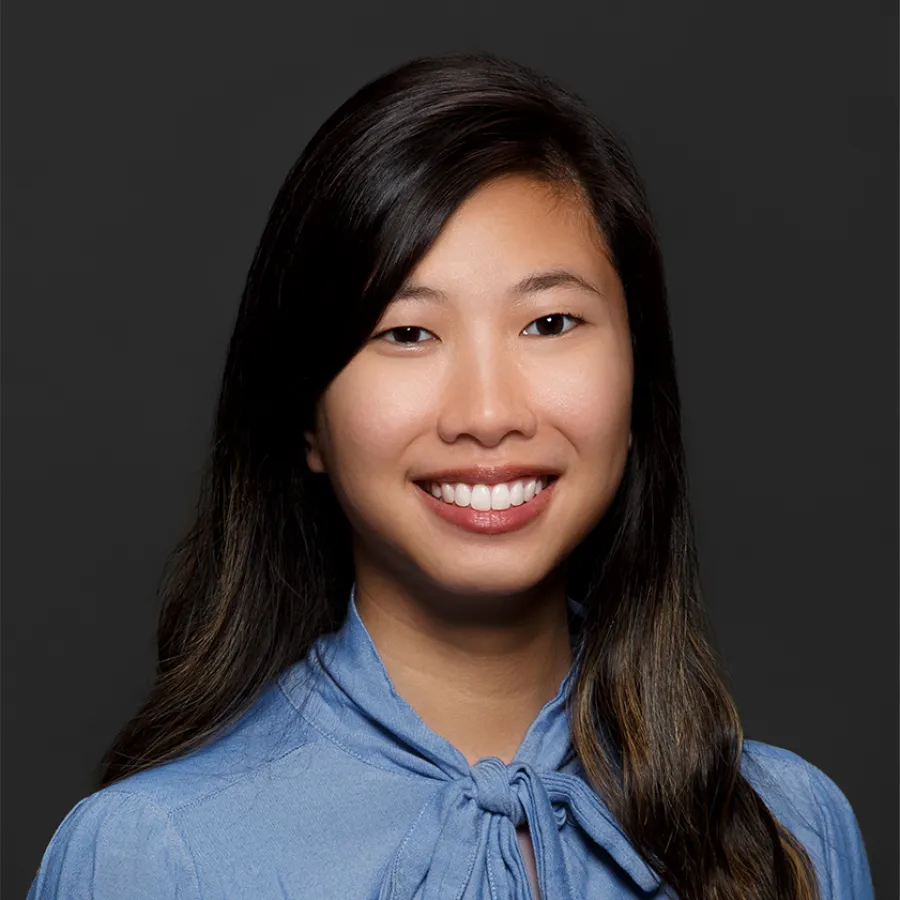 Portrait of smiling young woman with long dark hair wearing a blue blouse against dark background