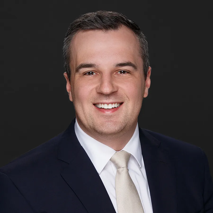 Smiling man in dark suit with white shirt and light tie against black background