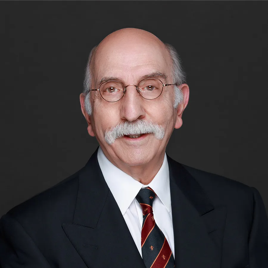 Portrait of an elderly man with a mustache and glasses wearing a suit and striped tie against a dark background