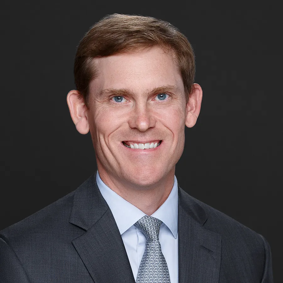 Portrait of a smiling man with blue eyes in a gray suit and patterned tie against a dark background