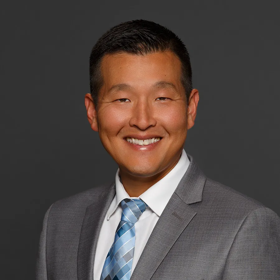 Smiling man in gray suit and blue striped tie against a dark gray background.