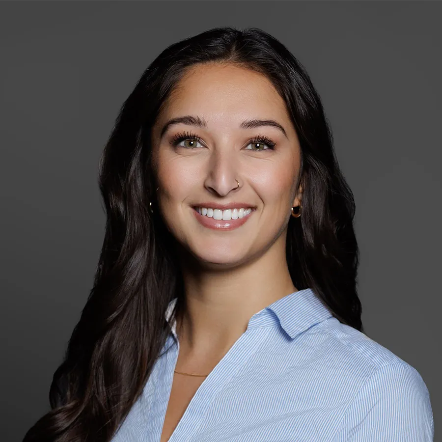 Young woman with long dark hair smiling in a light blue shirt against a dark gray background