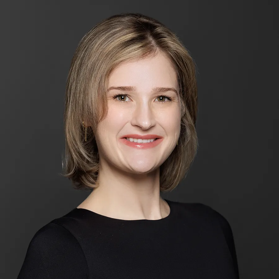 Smiling young woman with short blonde hair wearing a black top against a dark gray background