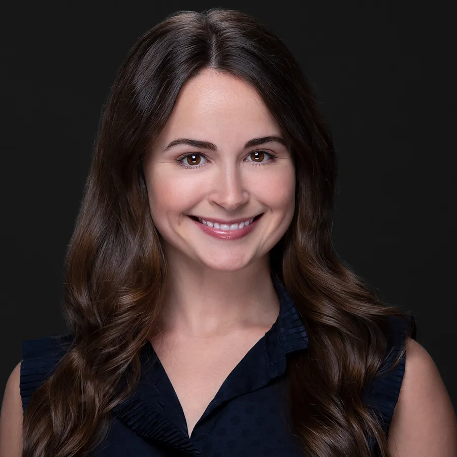 Smiling young woman with long brown hair and dark blouse against black background, professional portrait style