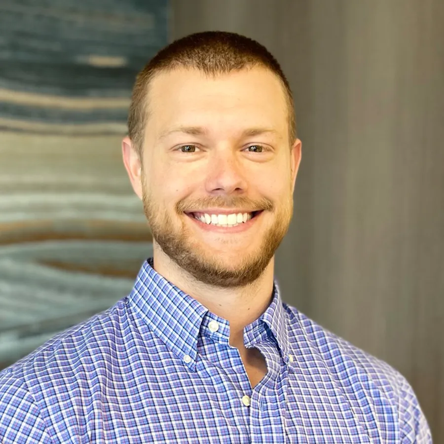 Smiling man with short hair and beard wearing a blue checkered shirt against a blurred background.