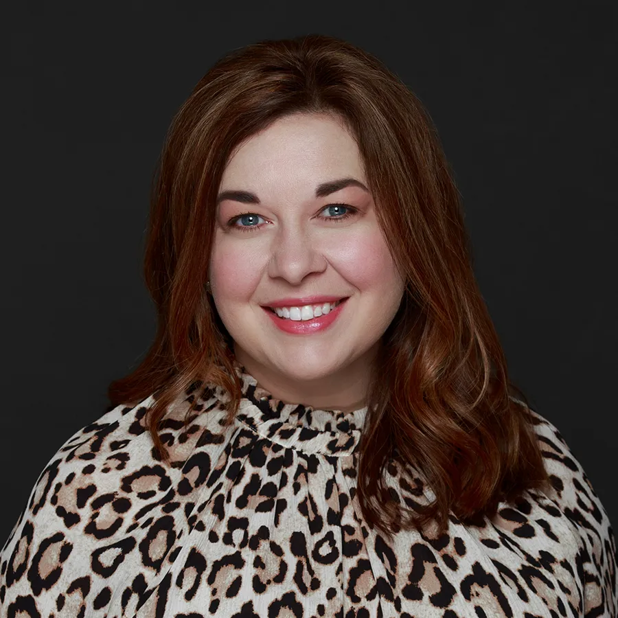 Smiling woman with red hair wearing a leopard print blouse against a black background