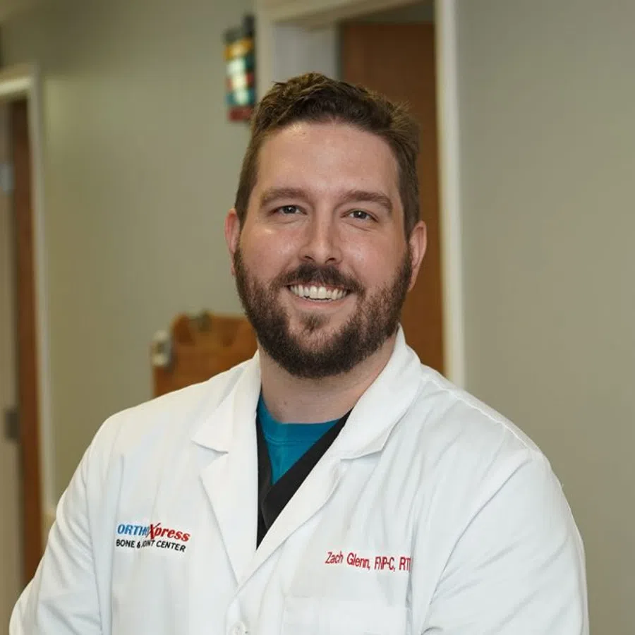 Smiling male medical professional in white coat standing in clinic hallway with blurred doors in background