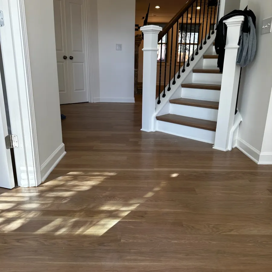 Wooden staircase and light hardwood floor in a modern home interior with white walls and closed door.