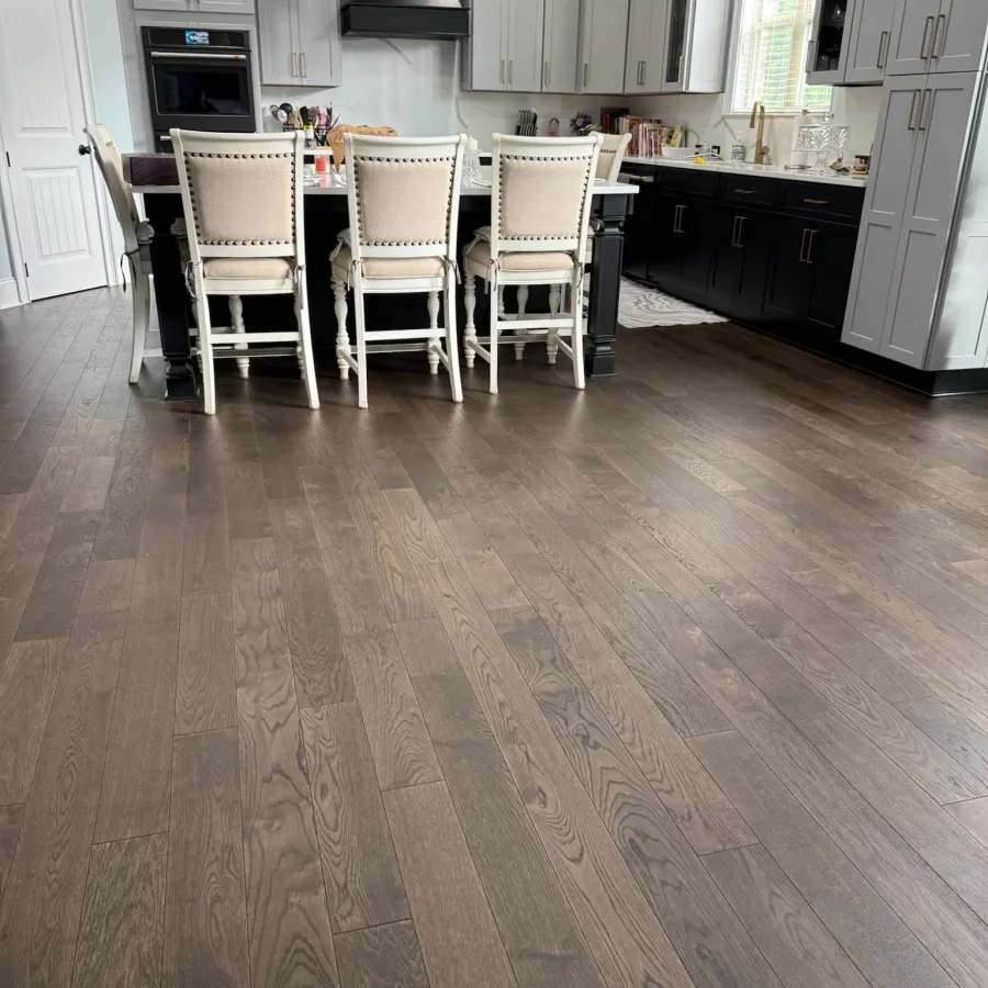 Modern kitchen with dark hardwood floors, white and black cabinets, and beige upholstered chairs at island.
