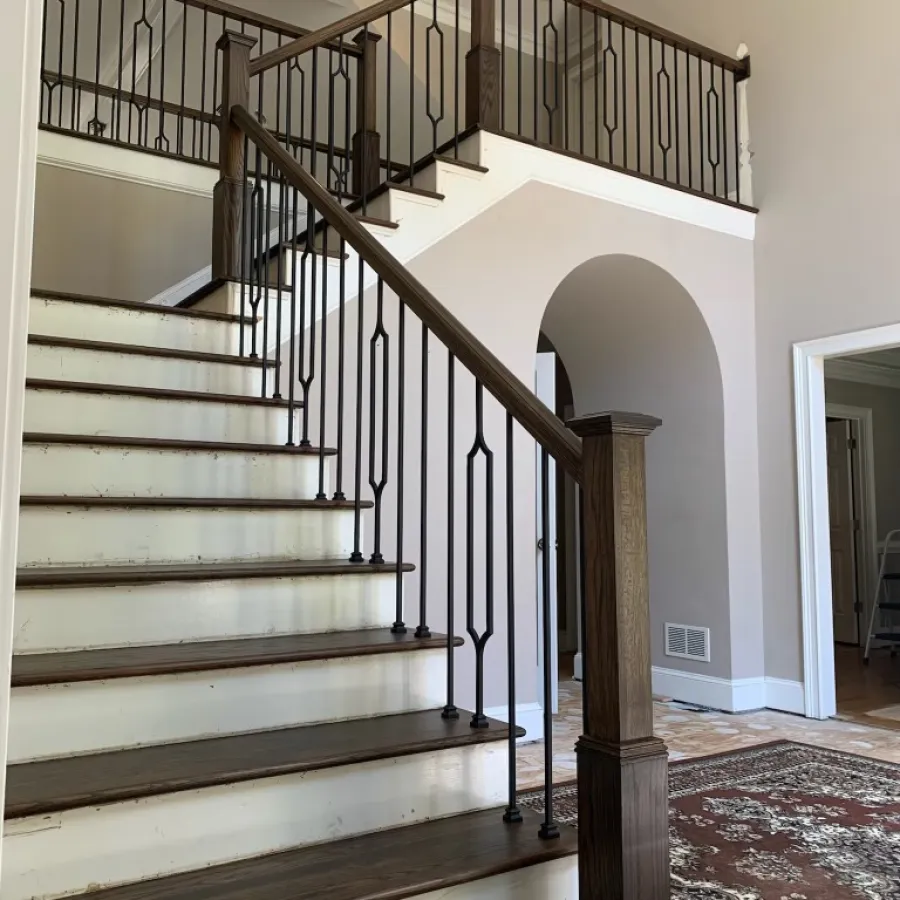 Interior view of a staircase with dark wood steps, black iron railing, beige walls, and an arched doorway.