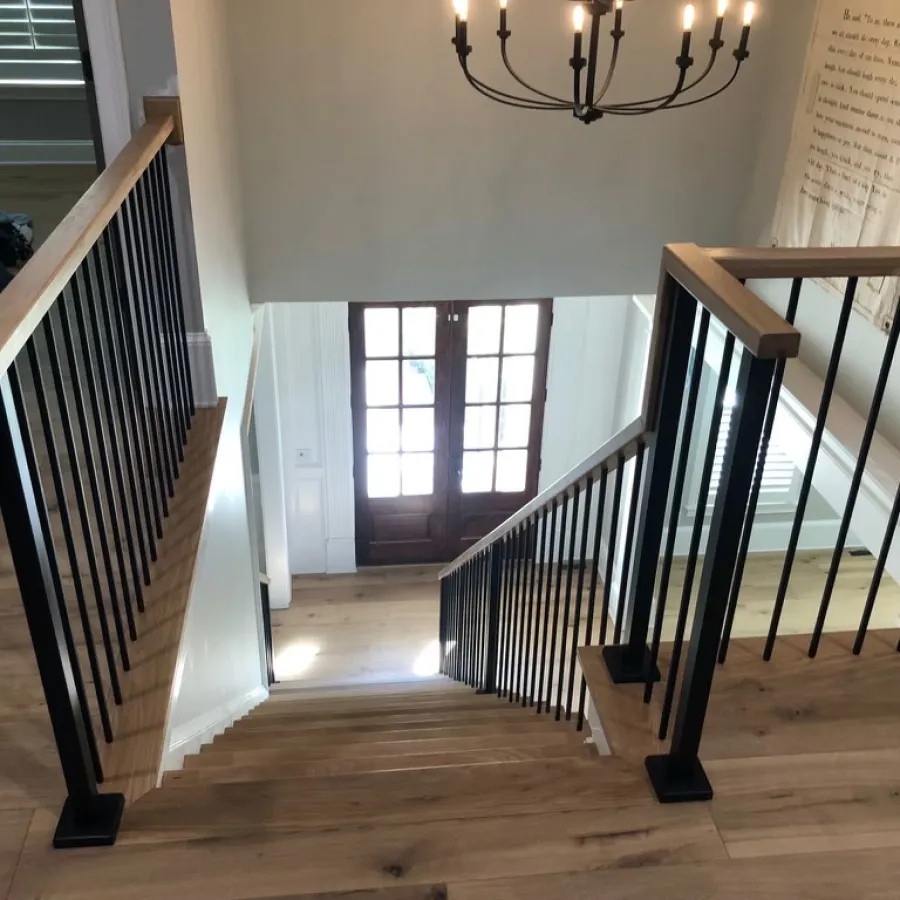 Wooden staircase with black metal balusters and a chandelier above in a modern home entryway