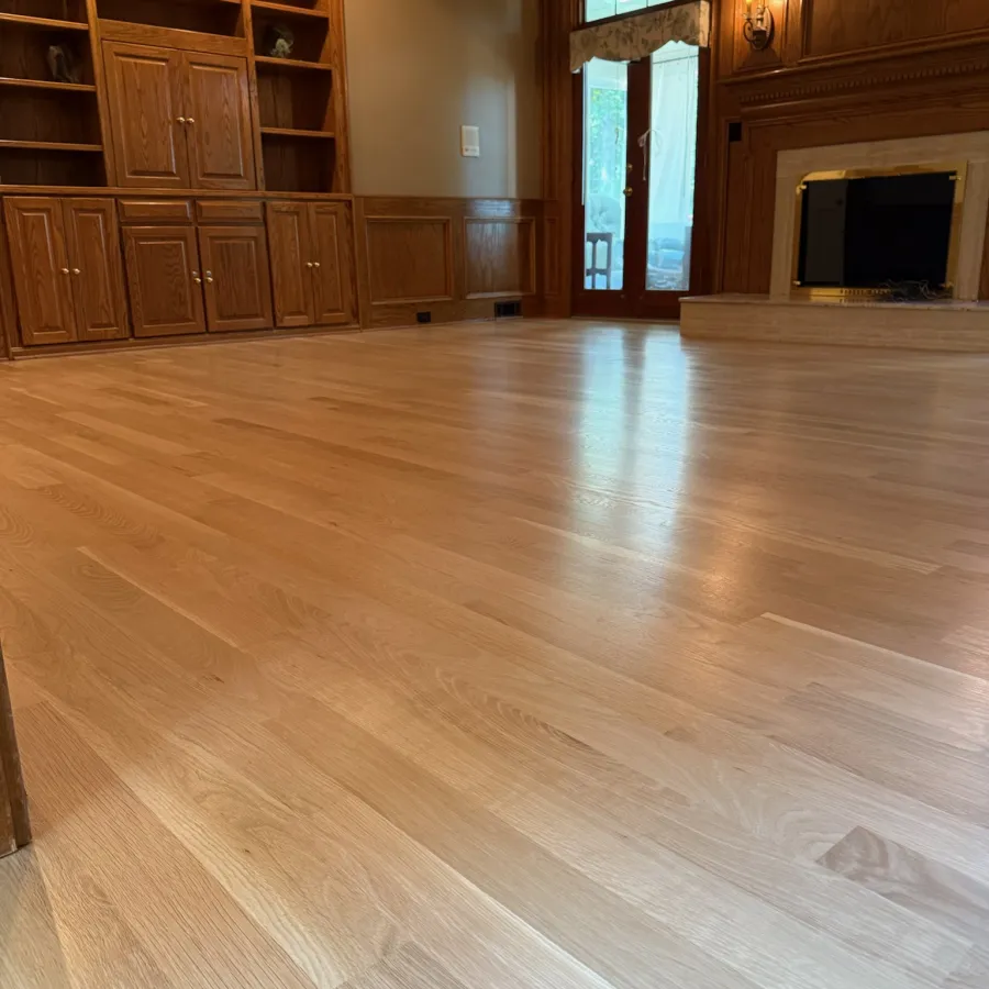 Glossy hardwood floor in a wood-paneled room with built-in shelves, fireplace, and glass double doors.