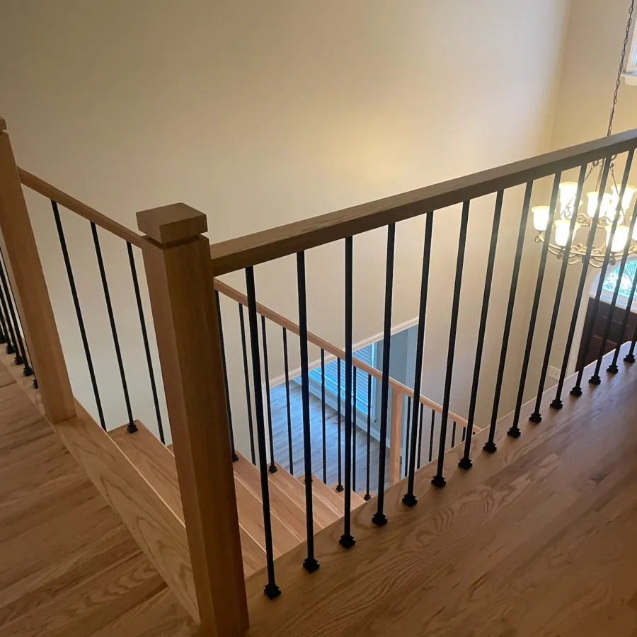 Wooden staircase railing with black metal balusters in a modern home interior with hardwood flooring.