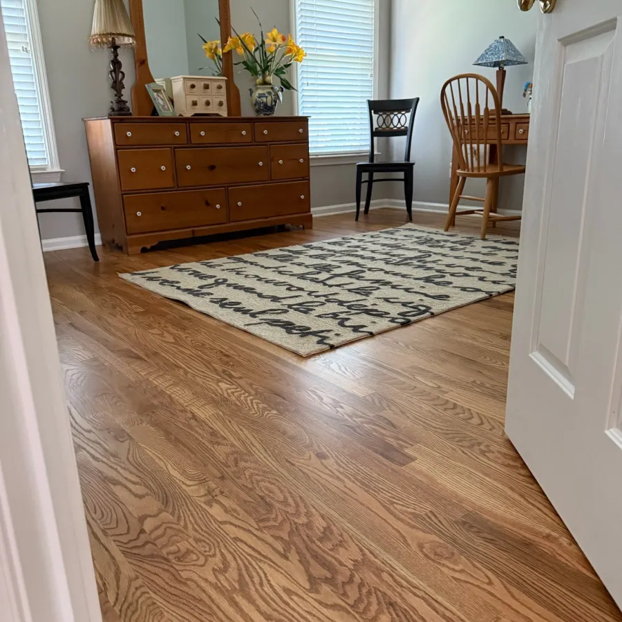 Bright room with wood floor, wooden dresser, decorative rug, two chairs, and a large mirror.