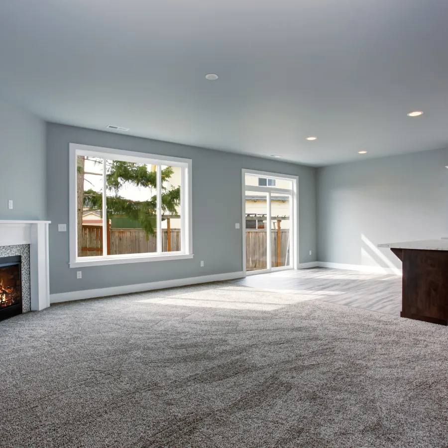 Spacious living room with carpet flooring, modern fireplace, large windows, and open kitchen with island and white cabinets.