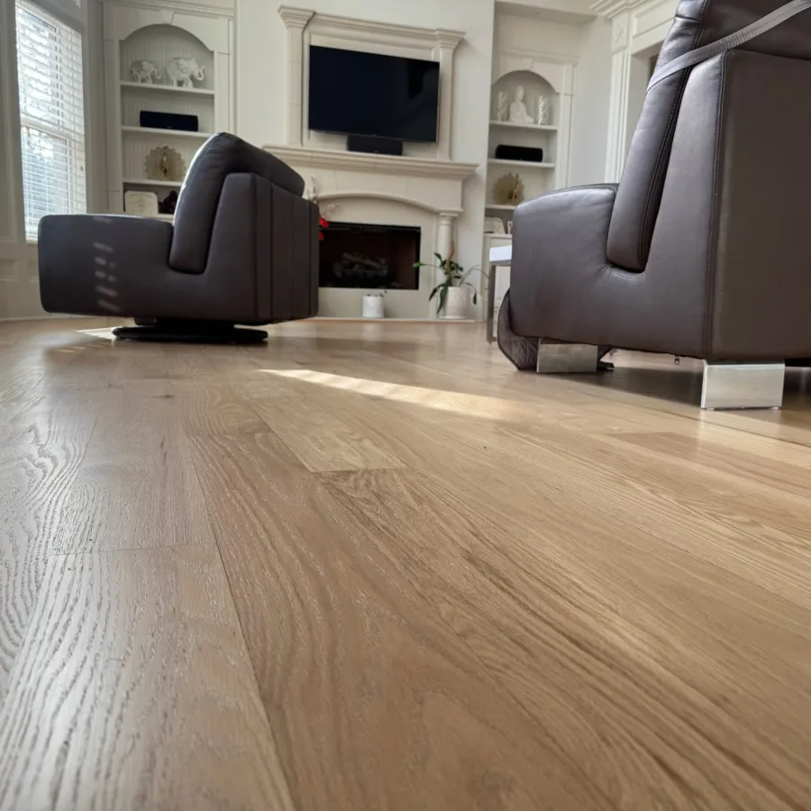Modern living room with light hardwood flooring, brown leather chairs, and a white fireplace with TV above.