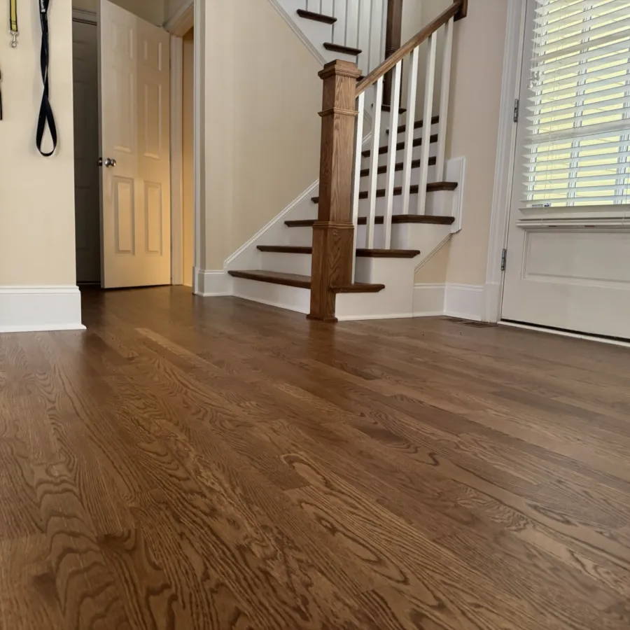 Bright entryway with dark hardwood floors, wooden staircase, white walls, and a door with window blinds.