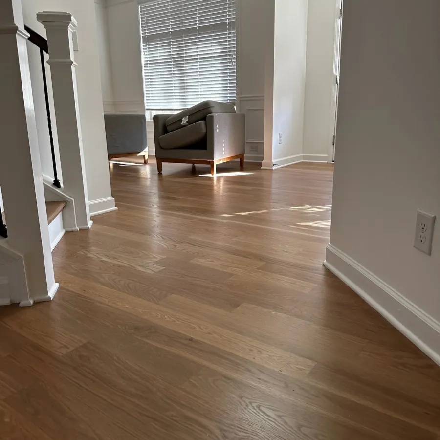 Sunlit modern living room with light hardwood floors, gray armchair, white walls, and window blinds.