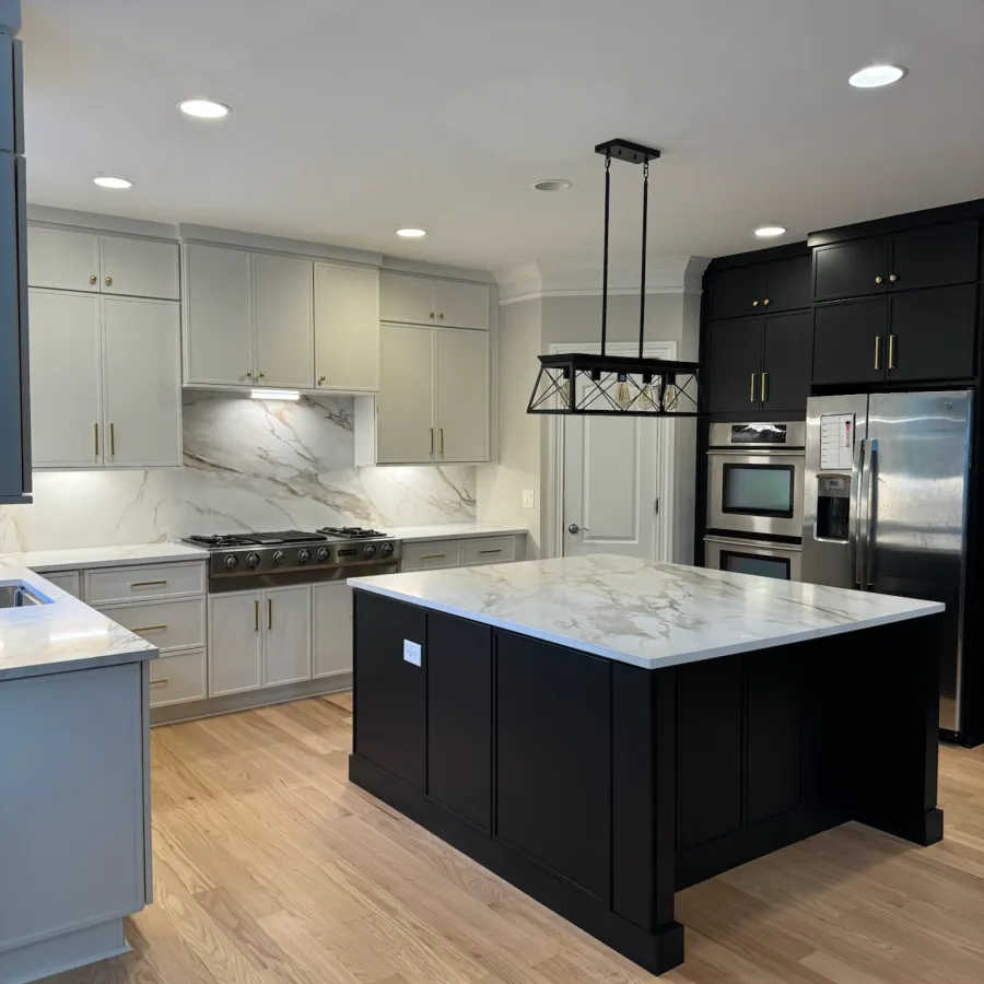 Modern kitchen with black and white cabinets, marble countertops, island, stainless steel appliances, and hardwood floors.