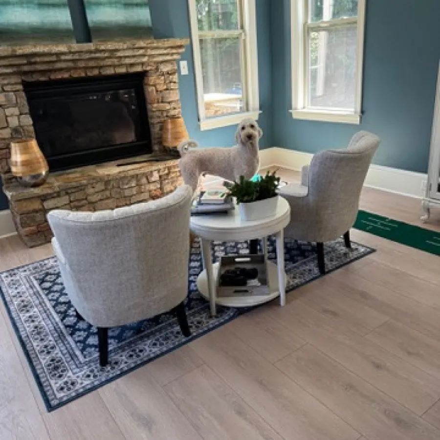 Cozy living room with stone fireplace, two gray armchairs, round table, rug, and a small dog standing inside.