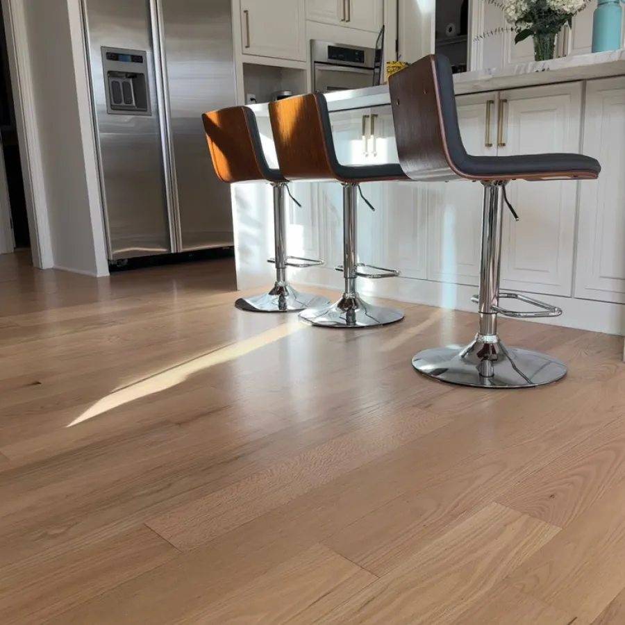 Modern kitchen with light wood flooring, white cabinetry, stainless steel appliances, and three wooden bar stools.