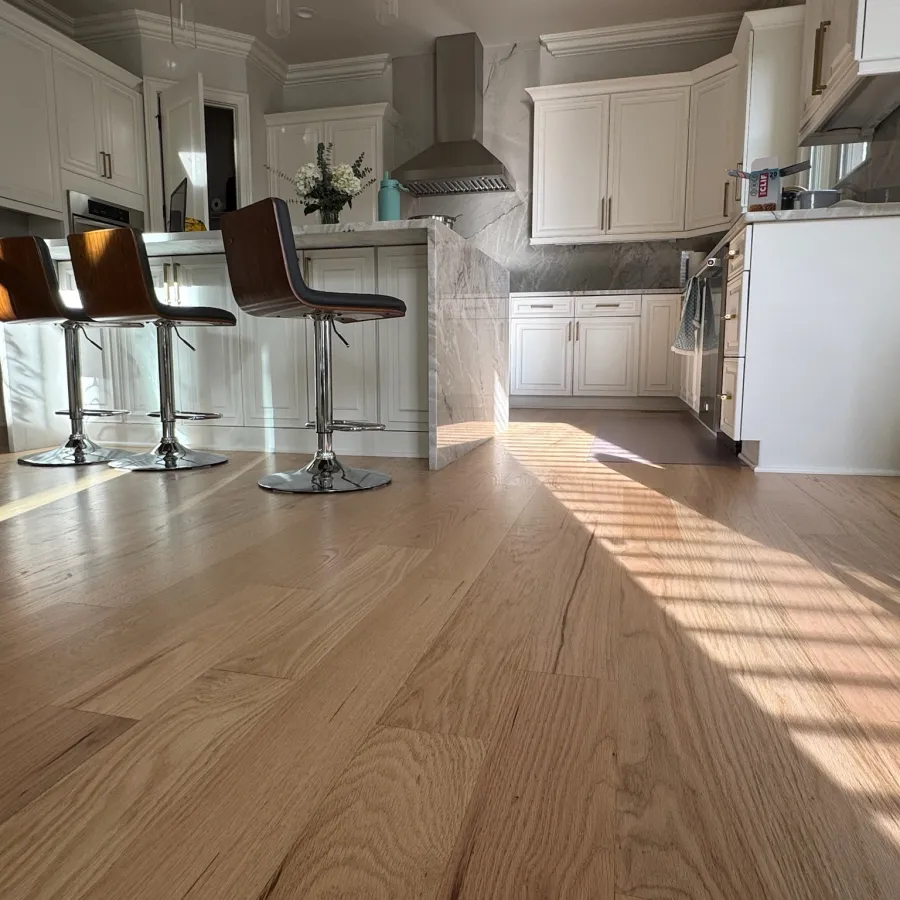 Modern kitchen with white cabinetry, wooden bar stools, stainless steel appliances, and natural light on hardwood floors