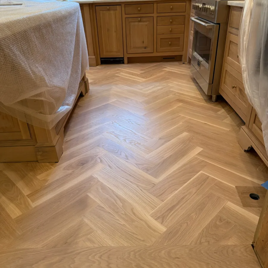 Newly installed herringbone pattern wooden floor in a kitchen with natural wood cabinets and covered countertops.