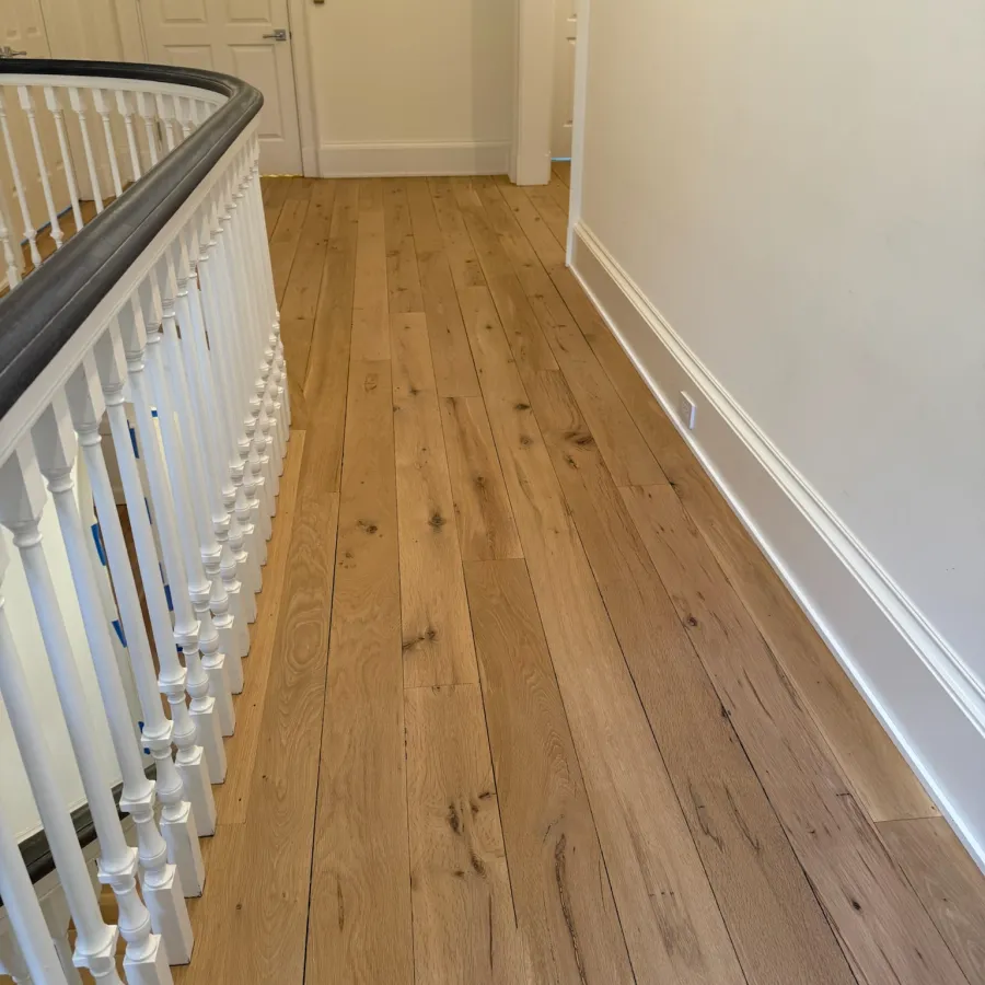 Bright hallway with light wooden floorboards, white walls, and white balustrade with gray handrail.
