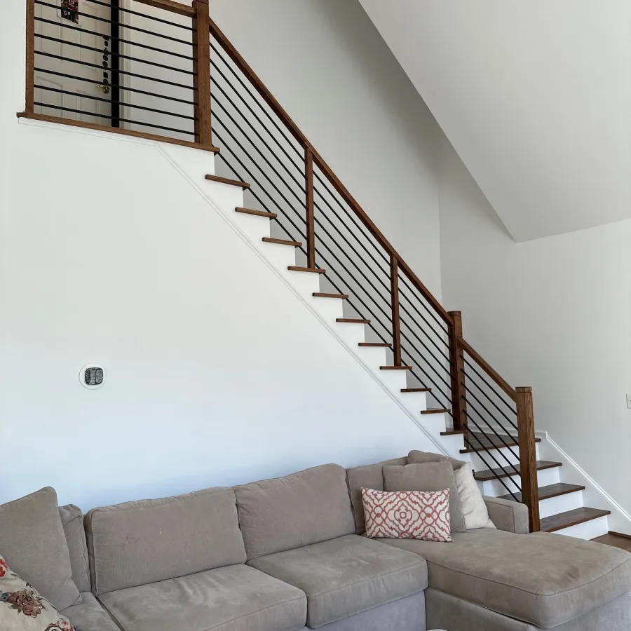 Modern living room with gray sectional sofa, patterned pillows, wooden tray, and staircase with wood and metal railing.