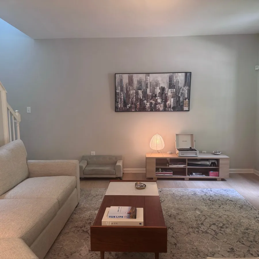 Bright living room with beige sofa, modern coffee table, rug, media console, and cityscape wall art under soft lighting.