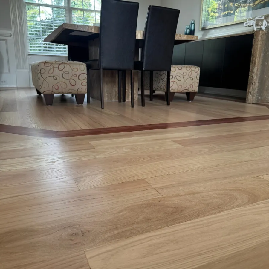 Modern dining room with light wood flooring featuring a decorative inlay and black leather chairs at a wooden table.