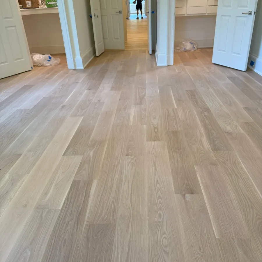 Newly installed light wood parquet flooring in a room with open white doors and shelving units.