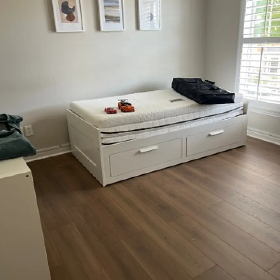 Minimalist bedroom with white trundle bed, framed abstract art, and hardwood floor under natural window light.