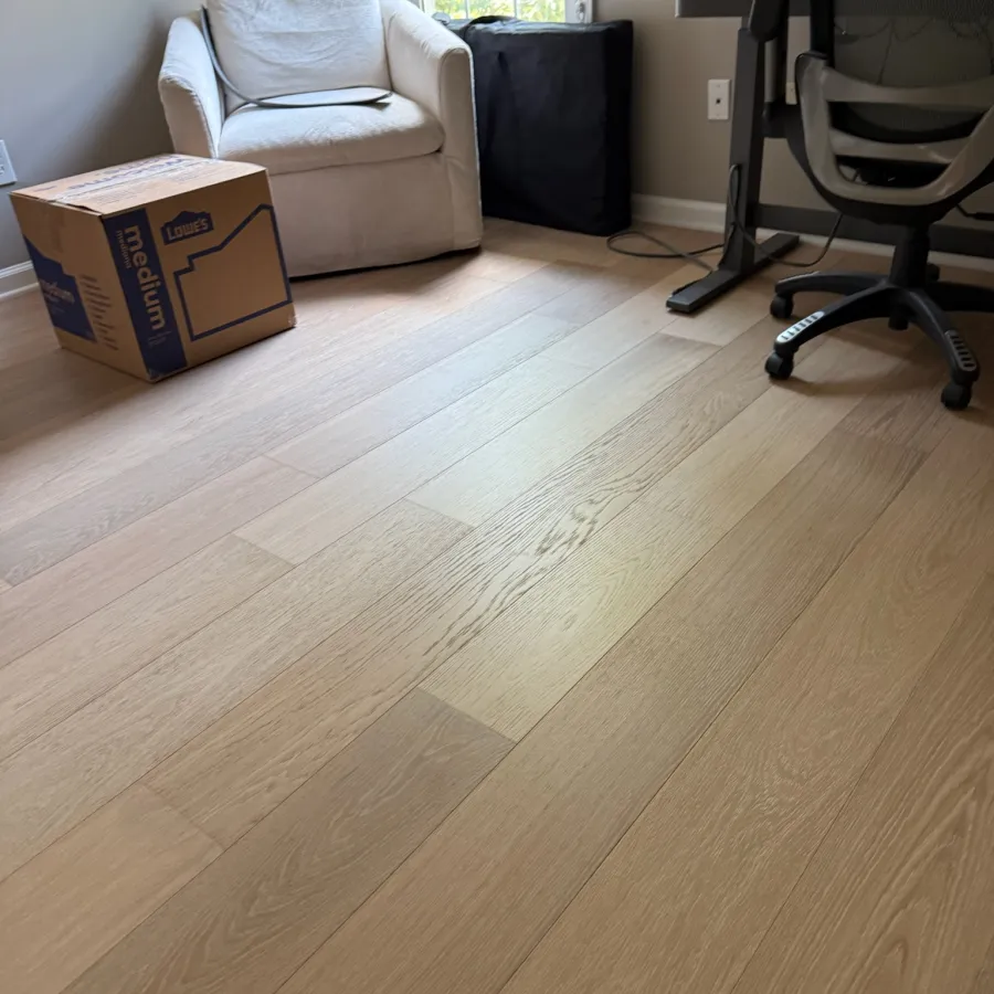 Bright home office corner with light wood flooring, white armchair, cardboard box, and black office chair.