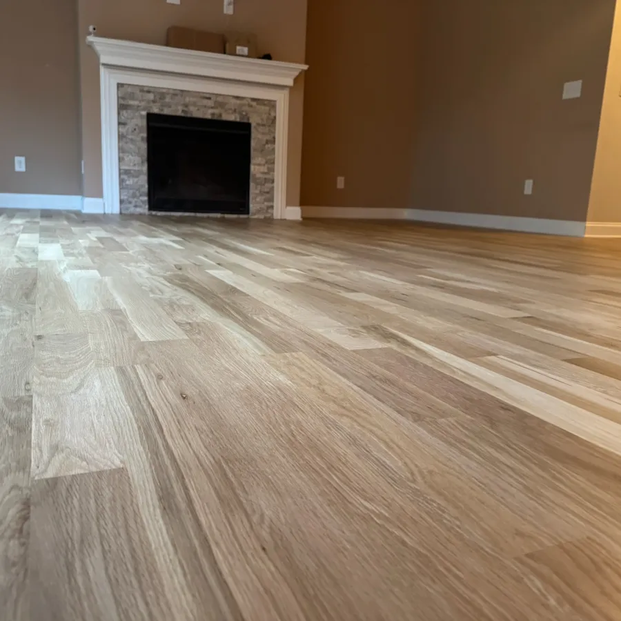 Low angle view of newly installed light wooden flooring with white fireplace and beige walls in empty room.