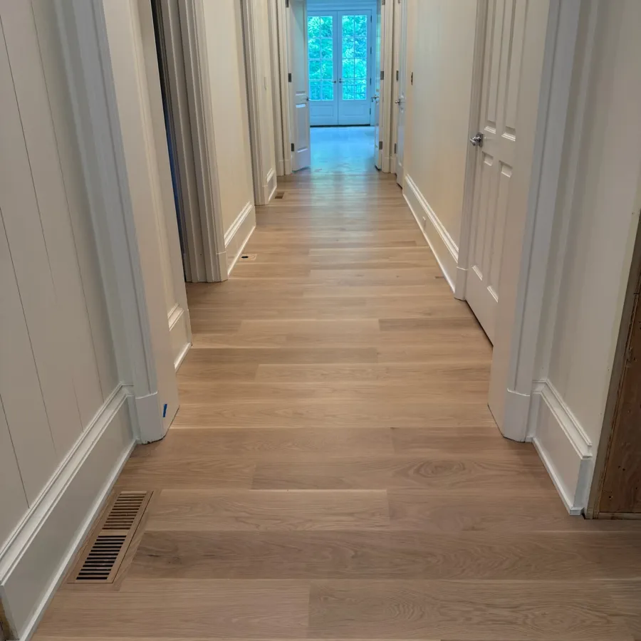 Bright hallway with light wood flooring, white walls, multiple doors, and a glass door at the end.