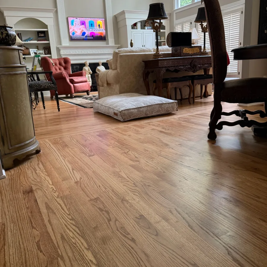 Spacious living room with hardwood floors, beige sofa, red armchair, large windows, and cozy decor.