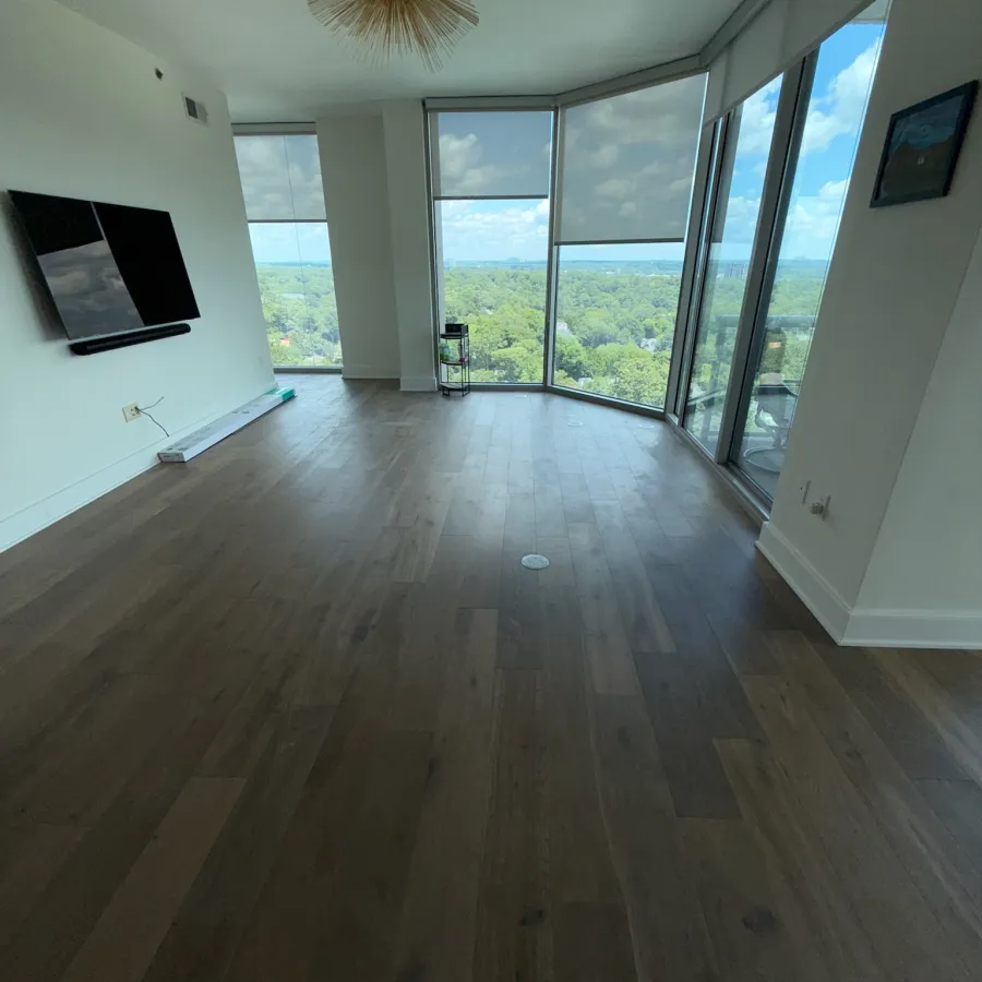 Empty modern living room with wood flooring, large windows, and a panoramic green landscape view outside.
