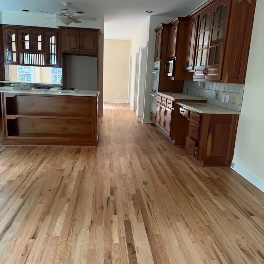 Spacious kitchen with wooden floors, dark wood cabinets, white ceiling, and built-in appliances along hall.