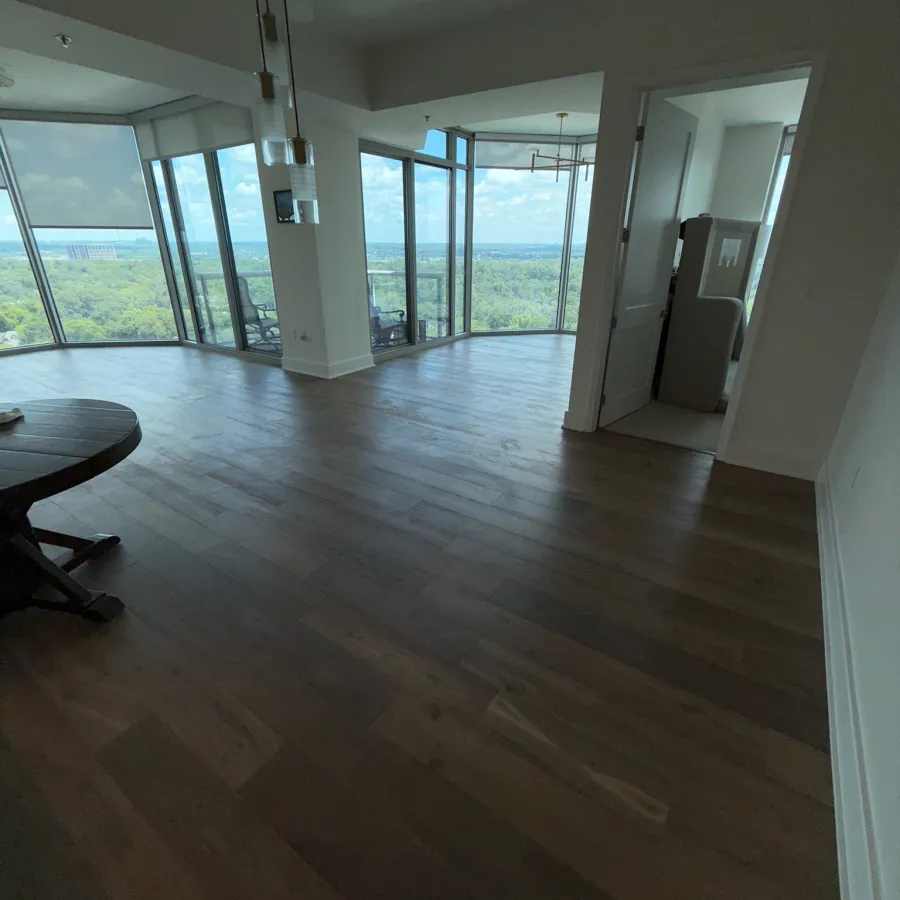 Spacious modern apartment with dark wood flooring and large windows offering panoramic forest and city views.