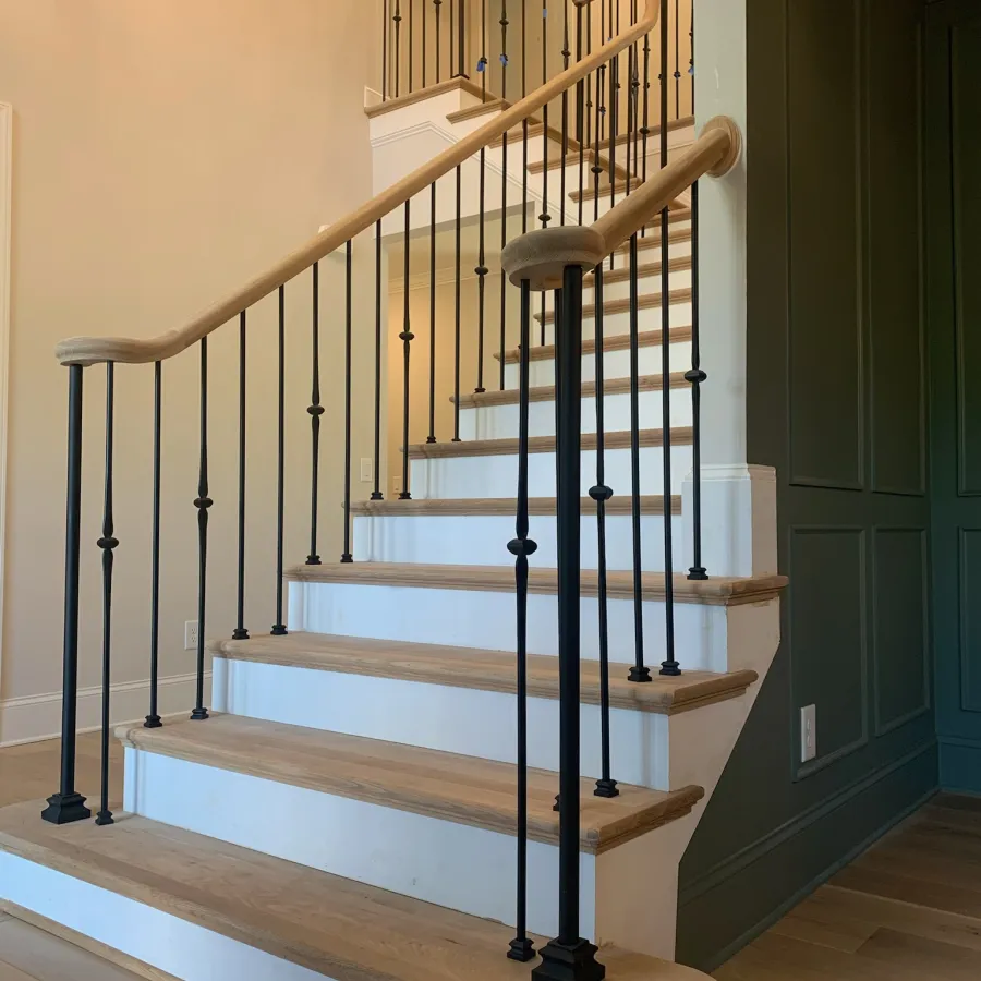 Indoor wooden staircase with black metal balusters and light-colored handrails in a modern home interior.