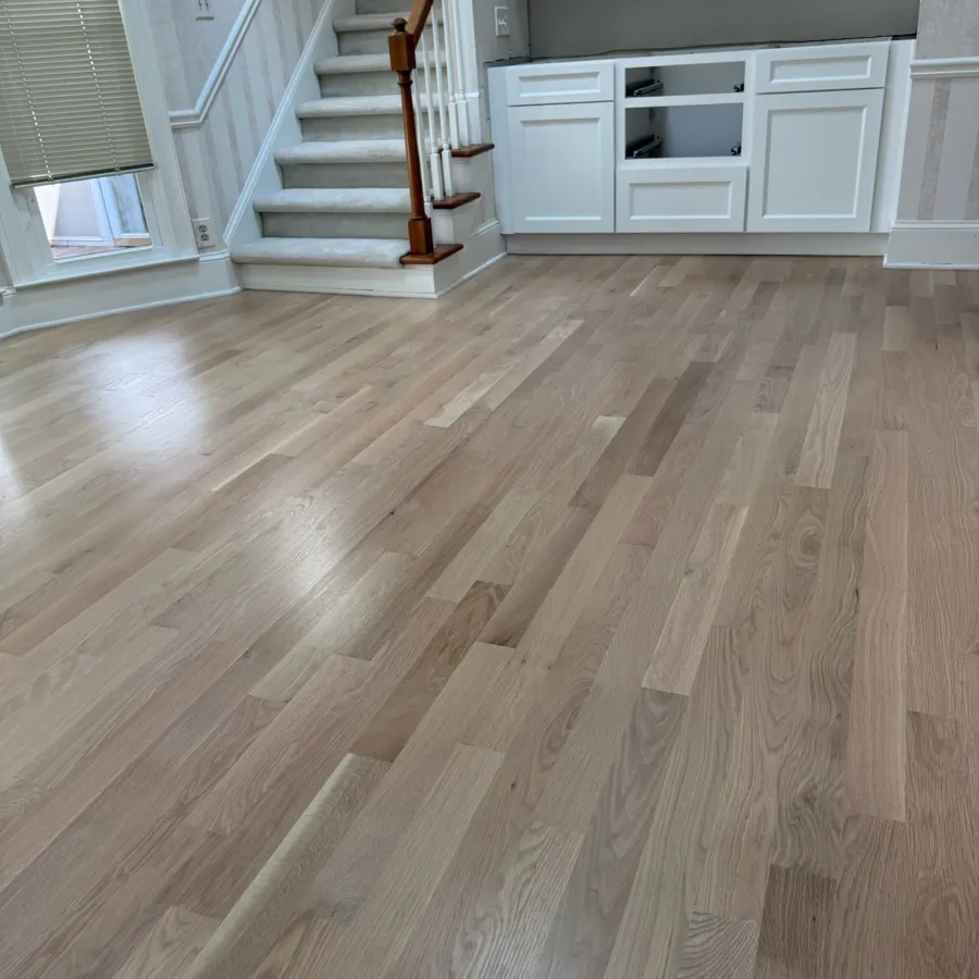 Newly installed light wood flooring in a bright room with white staircase and cabinetry.