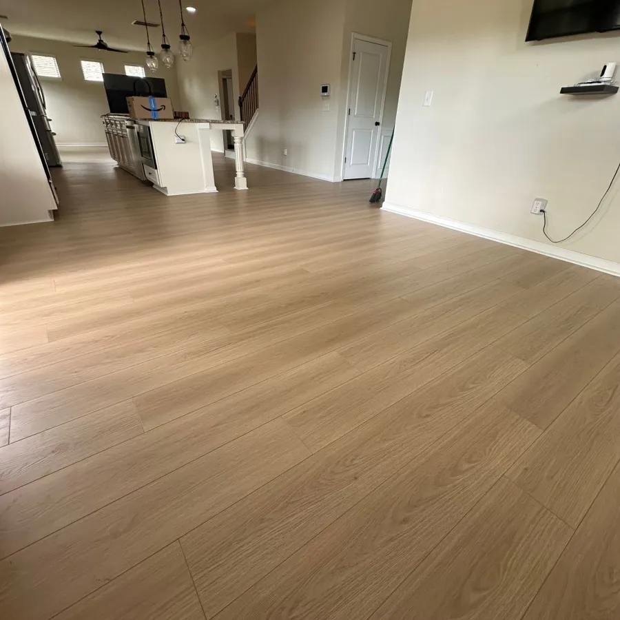 Spacious modern kitchen and living area with light wood flooring and neutral-colored walls under recessed lighting.