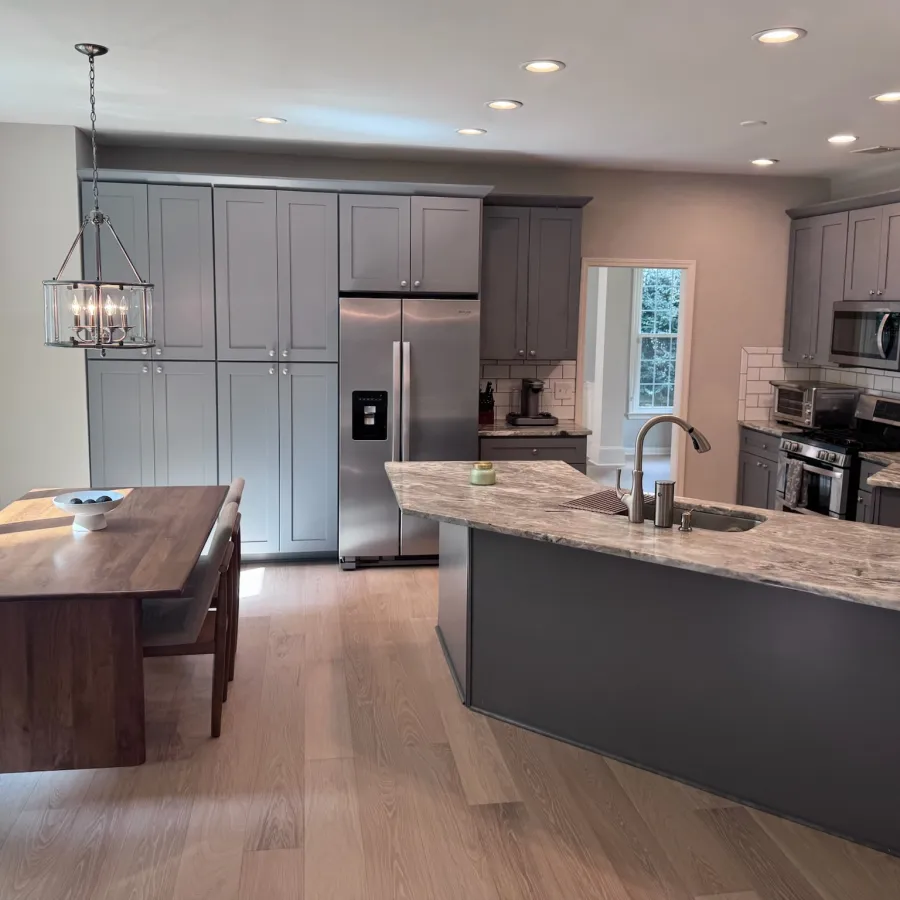 Modern kitchen with gray cabinets, stainless steel appliances, marble island countertop, and wooden dining table in natural light.