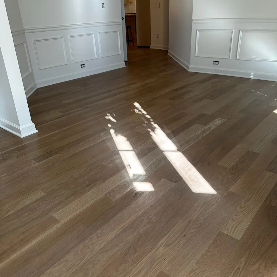 Empty room with light wood flooring, white wainscoted walls, and sunlight streaming through windows.
