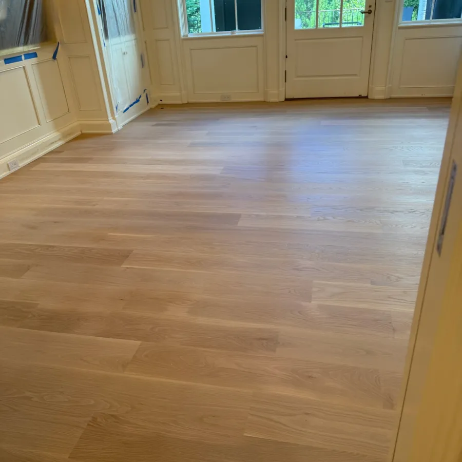 Newly installed light wooden flooring in a bright room with large windows and white walls.
