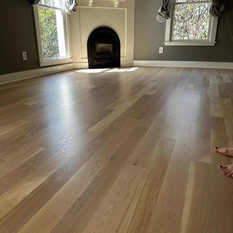 Empty room with light wooden floor, dark gray walls, large windows, white fireplace, and curtains tied back.