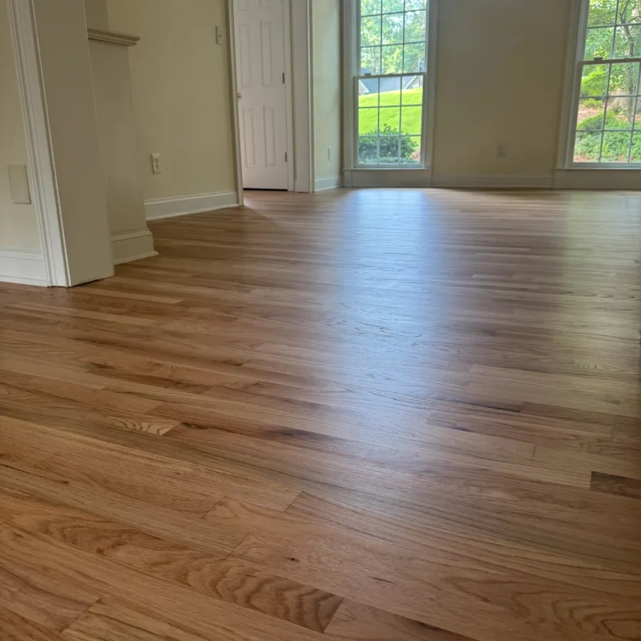 Empty room with natural light, light-colored walls, and polished hardwood flooring with large windows.